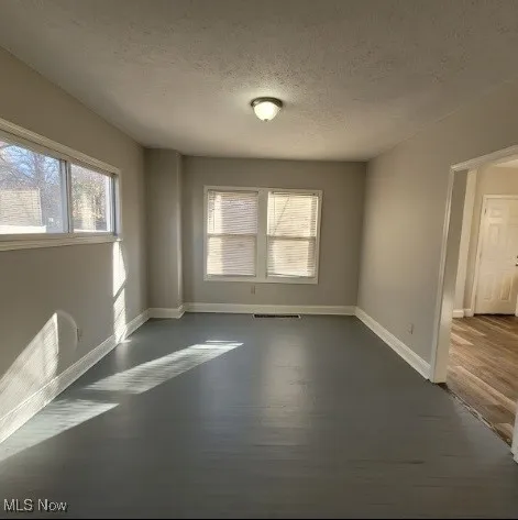 Unfurnished room with a textured ceiling, plenty of natural light, and dark wood finished floors