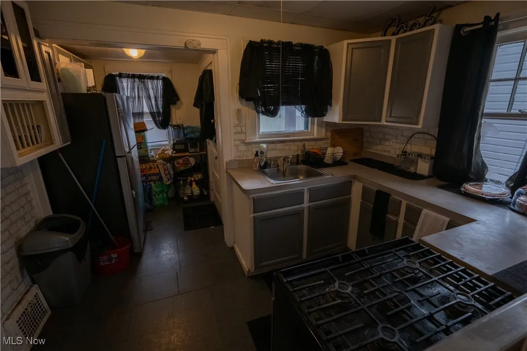 Kitchen with black gas cooktop, freestanding refrigerator, light countertops, white cabinets, and decorative backsplash