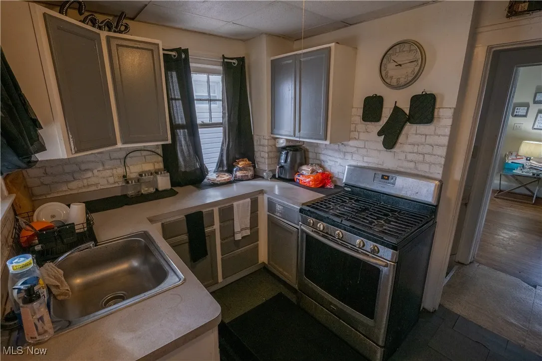 Kitchen featuring stainless steel range with gas cooktop, decorative backsplash, light countertops, white cabinetry, and a drop ceiling