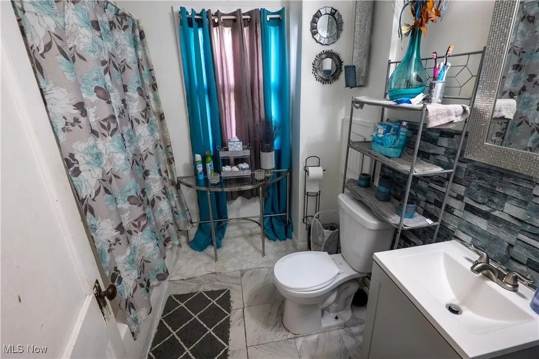 Full bath featuring curtained shower, vanity, and marble look tile flooring