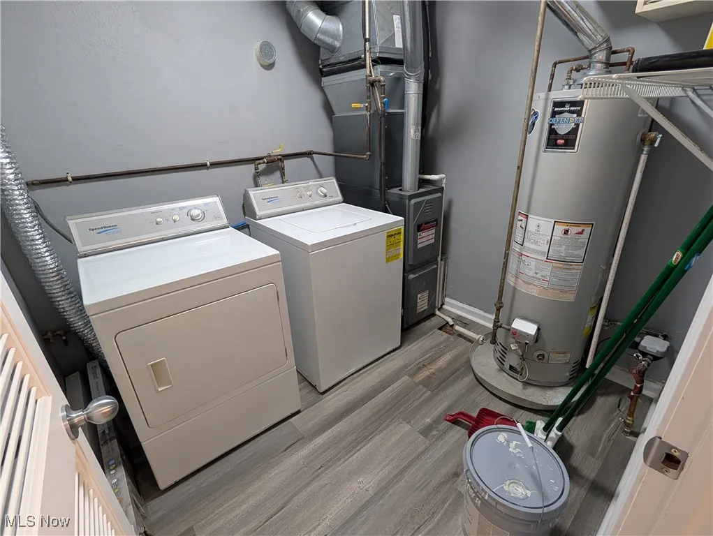 Washroom featuring water heater, washer and dryer, heating unit, and light wood-style floors