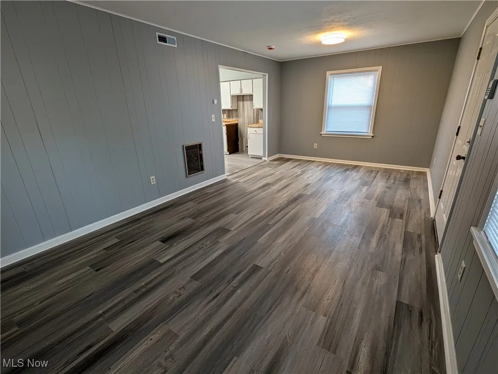 Unfurnished bedroom with dark wood-type flooring, wooden walls, and heating unit