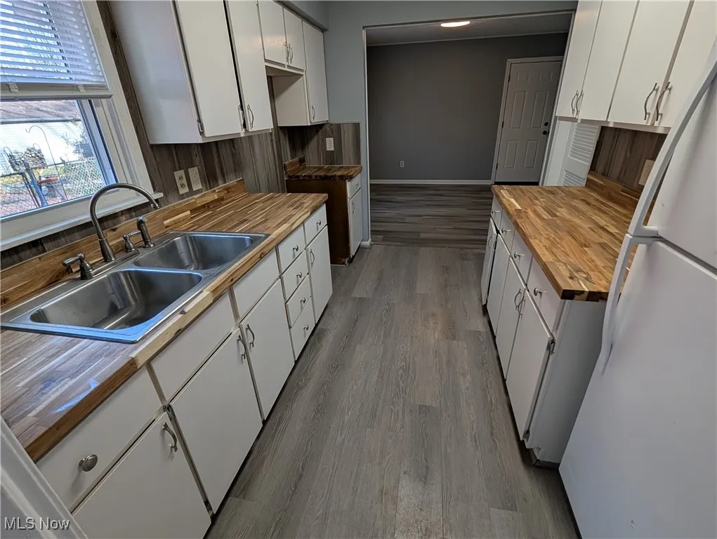 Kitchen featuring freestanding refrigerator, white cabinets, dark wood-type flooring, and butcher block counters
