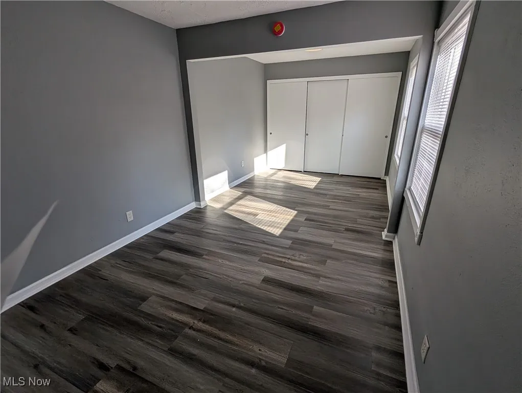 Primary bedroom on first floor with multiple windows, dark wood finished floors, a closet, and a textured ceiling