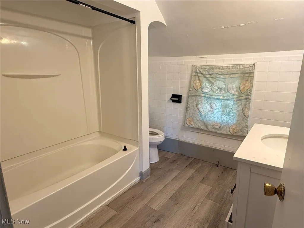Bathroom with vanity, tile walls, light wood-style floors, and shower / washtub combination