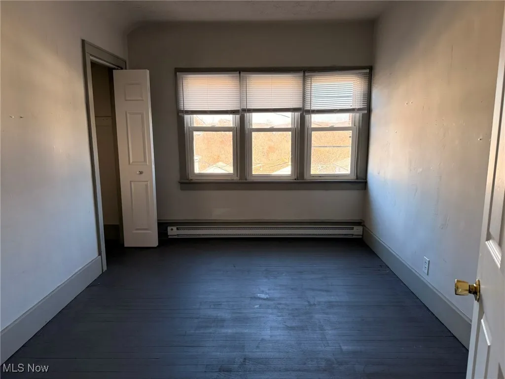 Unfurnished room with dark wood-style floors and baseboard heating