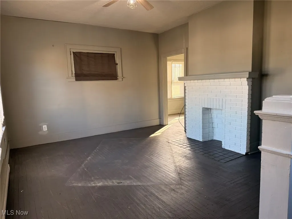 Unfurnished living room with a brick fireplace, dark wood-type flooring, and a ceiling fan