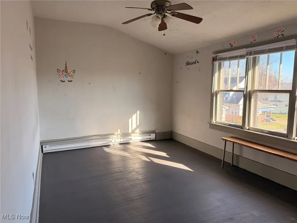Empty room featuring dark wood-style flooring, a baseboard heating unit, vaulted ceiling, and ceiling fan
