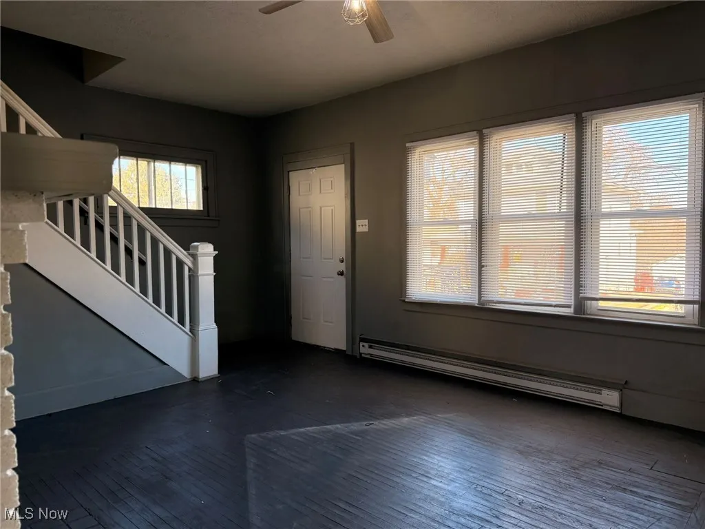 Entrance foyer with stairs, baseboard heating, dark wood-style flooring, and a ceiling fan