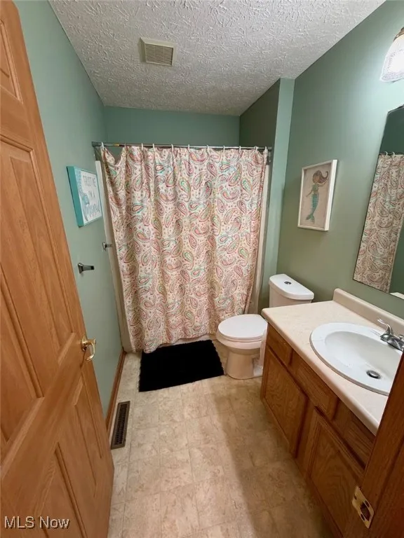 Bathroom featuring a shower with shower curtain, vanity, and a textured ceiling
