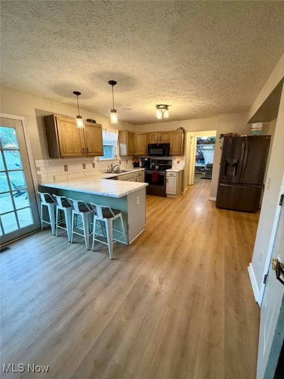 Kitchen with light countertops, a breakfast bar, a peninsula, black appliances, and decorative light fixtures