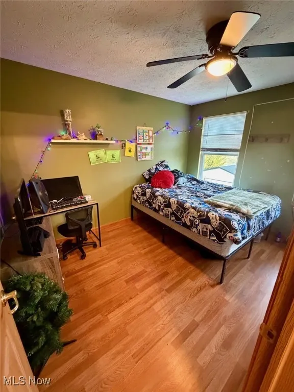 Bedroom with wood finished floors, a textured ceiling, ceiling fan, and a desk