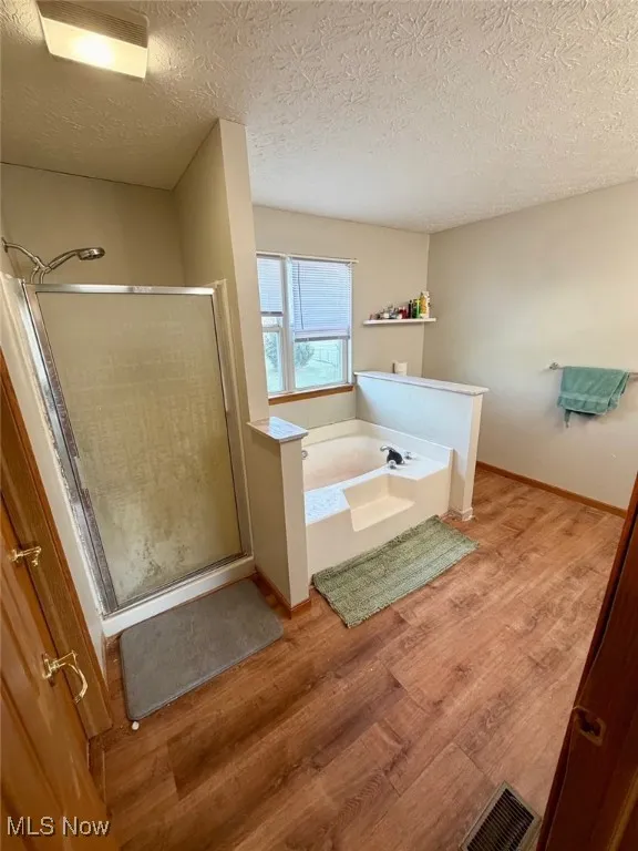 Bathroom featuring a stall shower, a bath, light wood-type flooring, and a textured ceiling