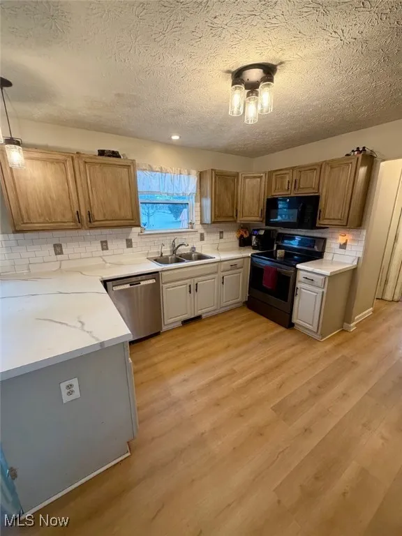 Kitchen featuring light countertops, appliances with stainless steel finishes, decorative light fixtures, a textured ceiling, and light wood-style flooring