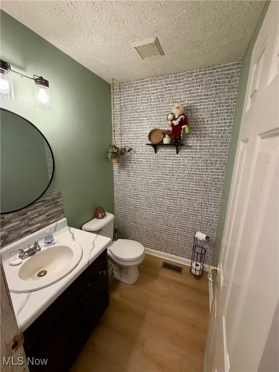Half bath featuring vanity, wood finished floors, an accent wall, and a textured ceiling