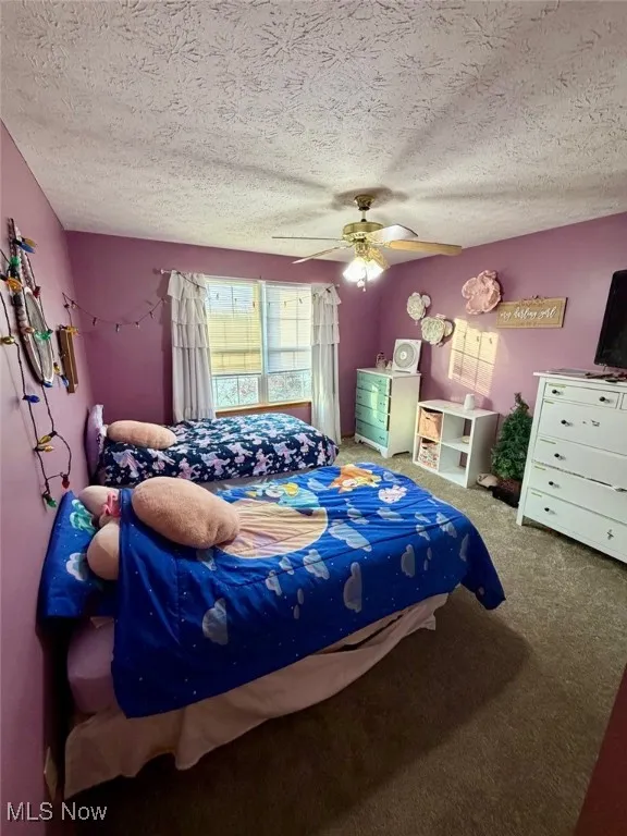 Carpeted bedroom with multiple windows, a ceiling fan, and a textured ceiling