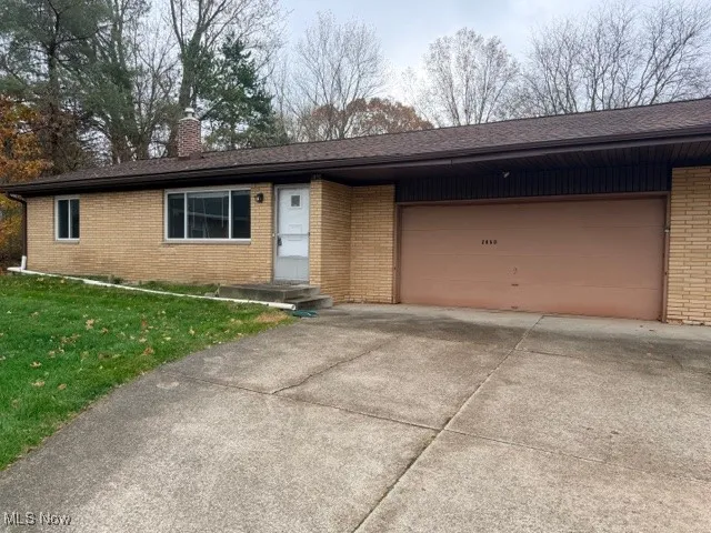 Ranch-style house with brick siding, a front lawn, driveway, a chimney, and an attached garage