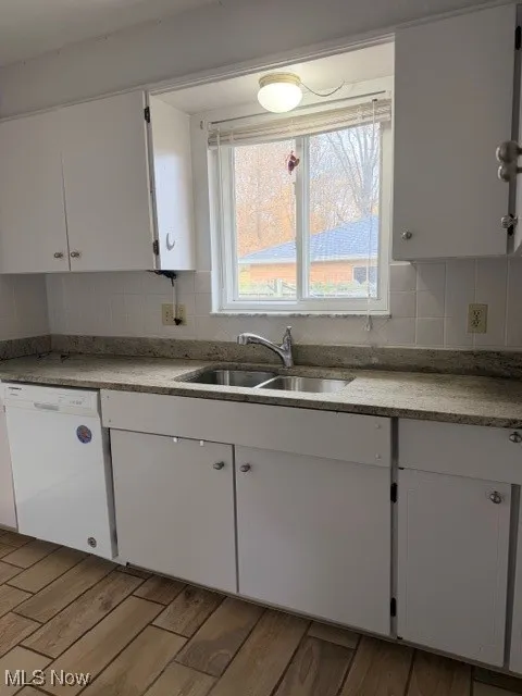 Kitchen featuring white cabinetry, backsplash, dishwasher, light wood-style flooring, and light countertops