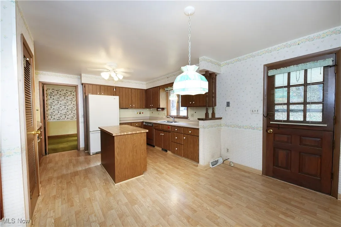 Kitchen with wallpapered walls, a center island, freestanding refrigerator, light countertops, and light wood-style floors