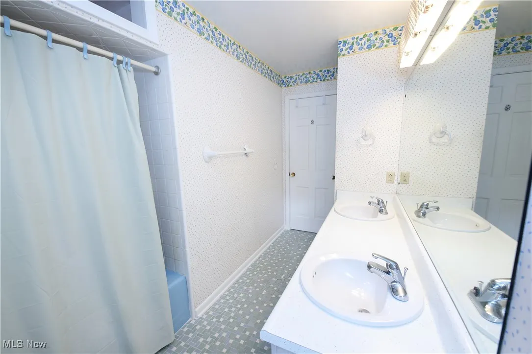 Full bath featuring double vanity, wallpapered walls, shower / bath combo, and tile patterned floors