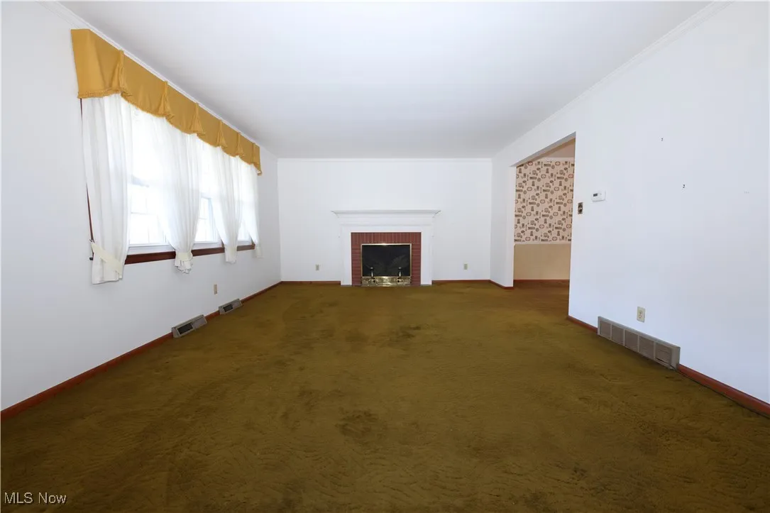 Unfurnished living room featuring a brick fireplace, dark colored carpet, and ornamental molding