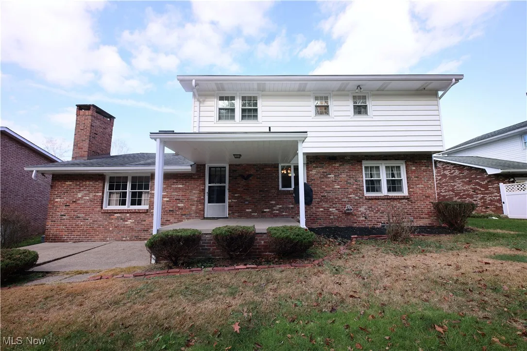 Back of house with a patio area, brick siding, a lawn, and a chimney
