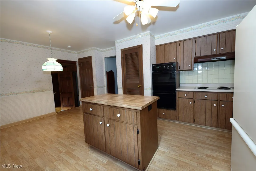 Kitchen with wallpapered walls, a kitchen island, white appliances, light countertops, and a wainscoted wall