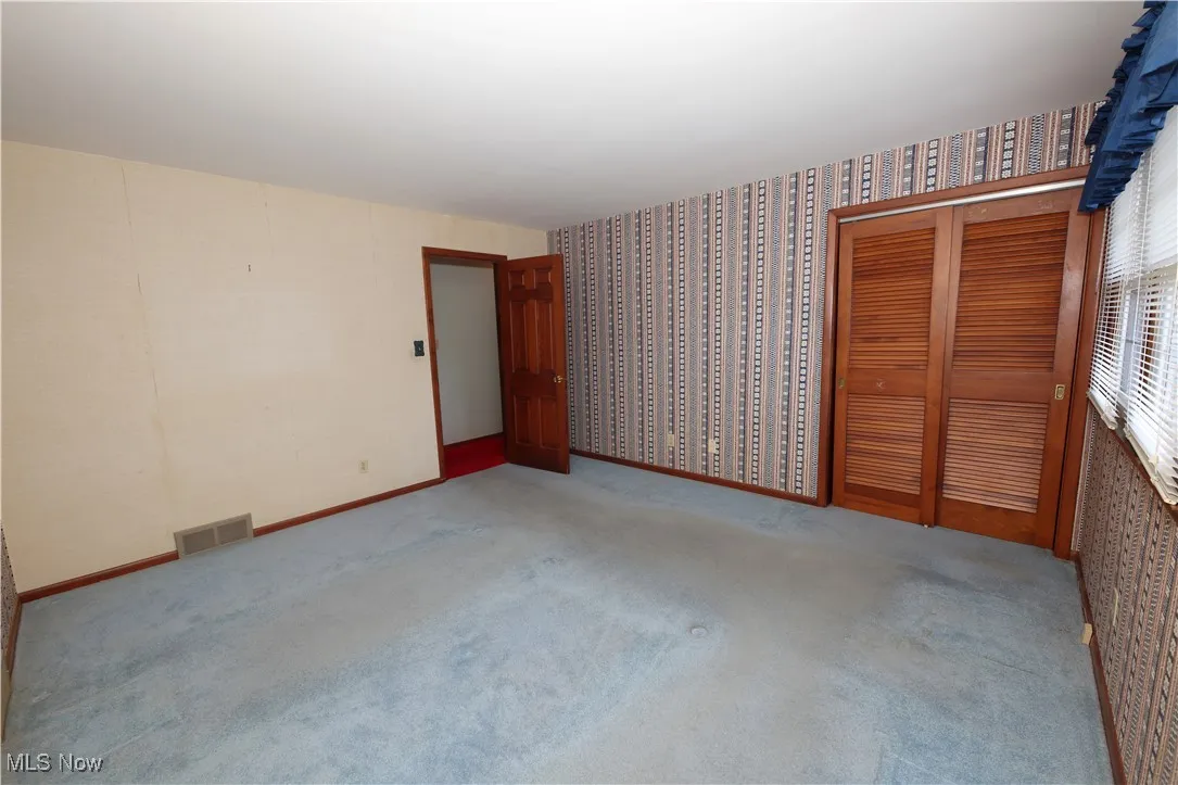 Unfurnished bedroom with wallpapered walls, carpet floors, and a closet