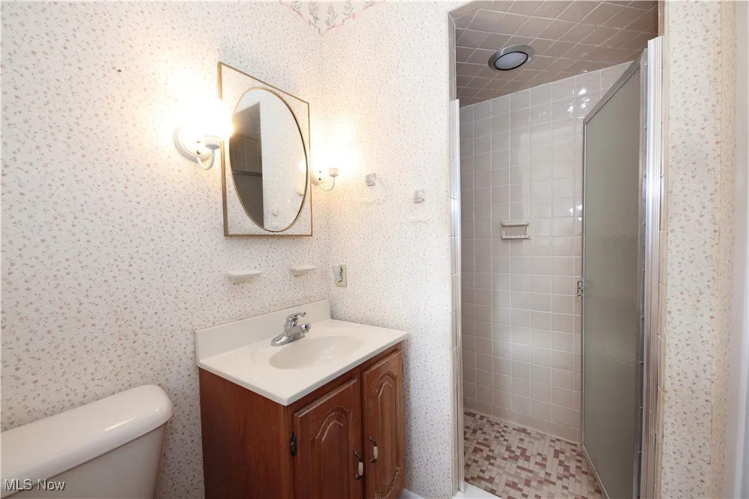 Full bath with a stall shower, wallpapered walls, and vanity