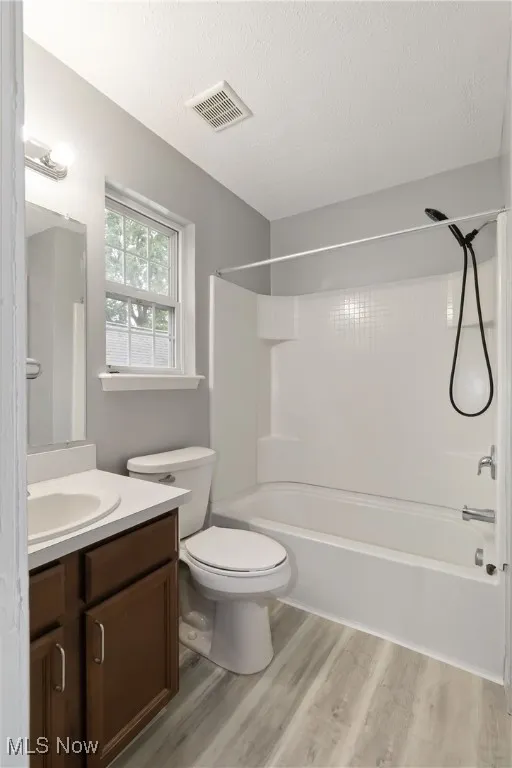 Full bath with tub / shower combination, a textured ceiling, vanity, and light wood-type flooring