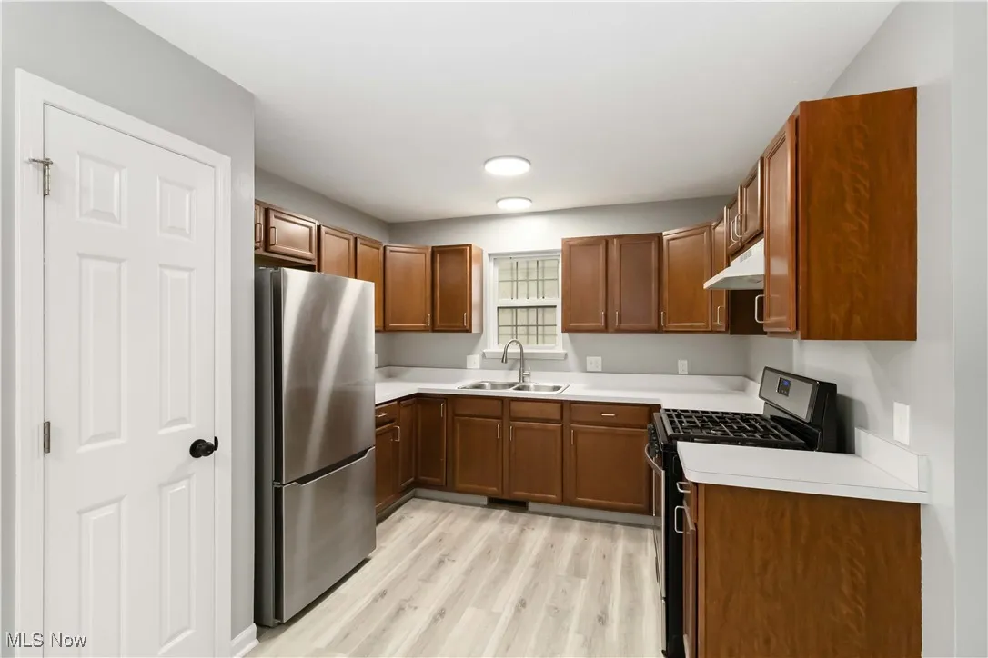 Kitchen with light countertops, gas range oven, freestanding refrigerator, brown cabinets, and light wood-type flooring
