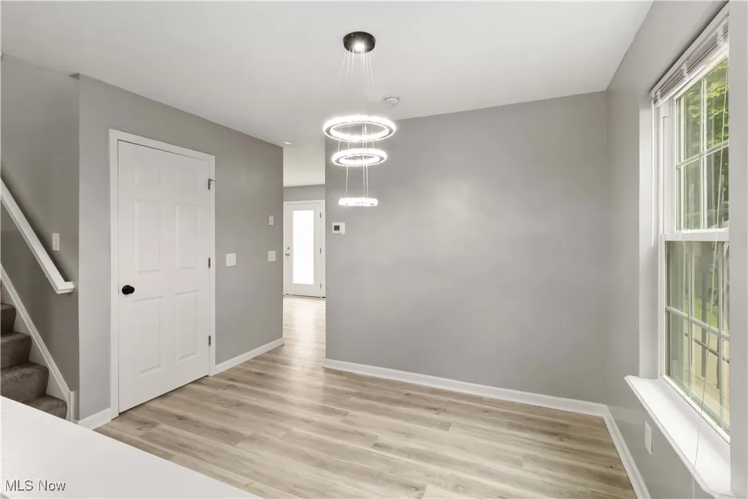 Unfurnished dining area with stairs, light wood-style floors, and a chandelier