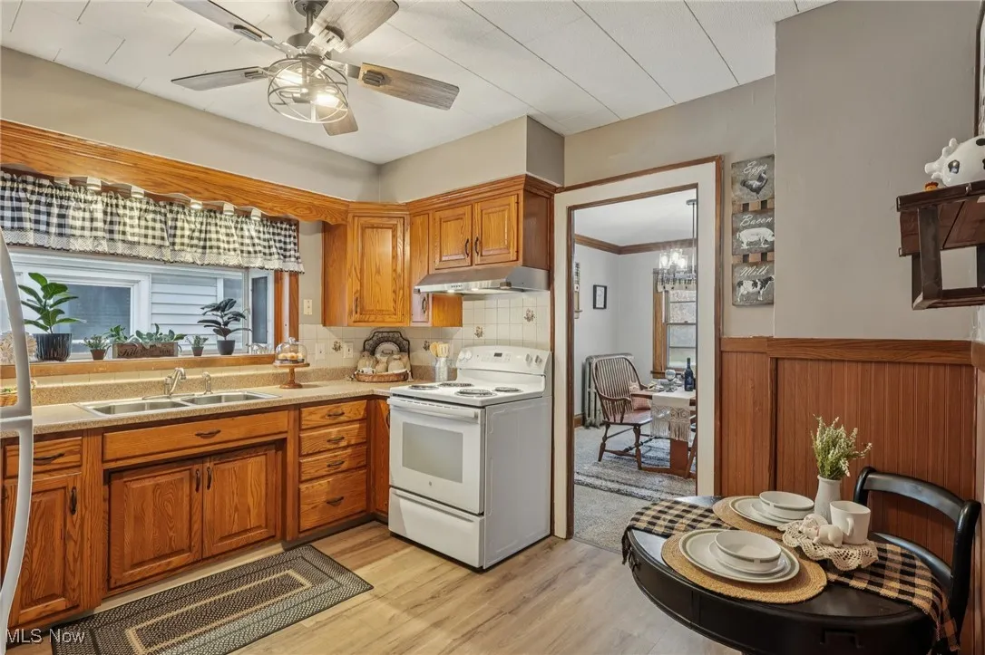 Kitchen with white electric range oven, brown cabinetry, light countertops, light wood-style floors, and tasteful backsplash