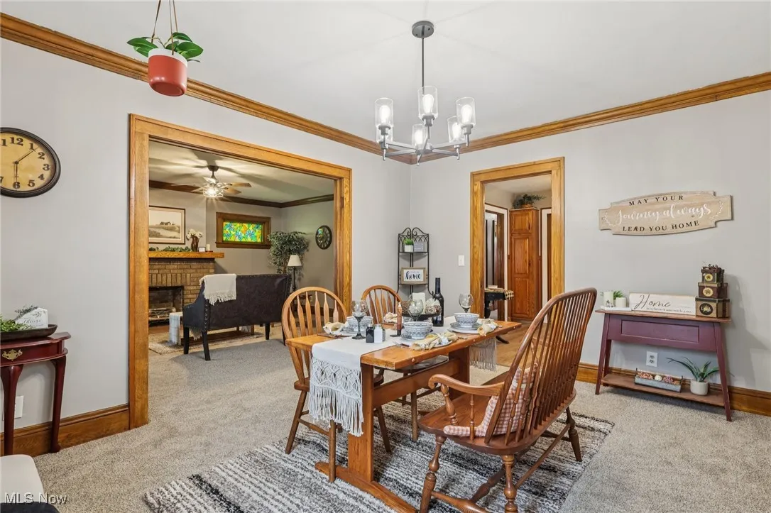 Dining room with ornamental molding, light carpet, a chandelier, a fireplace, and ceiling fan