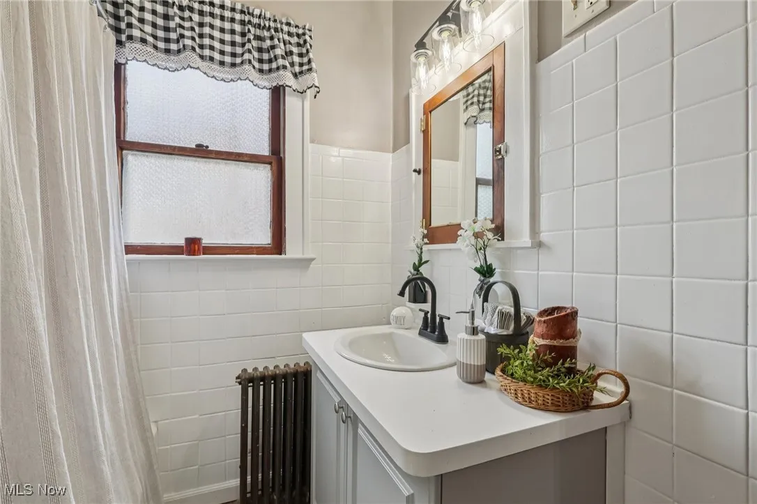 Bathroom featuring radiator heating unit, vanity, tile walls, and curtained shower