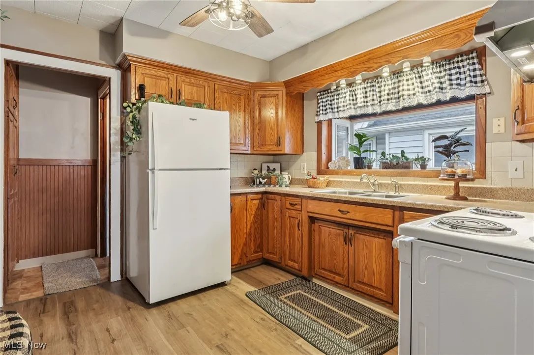 Kitchen with white appliances, brown cabinets, ventilation hood, light wood finished floors, and light countertops