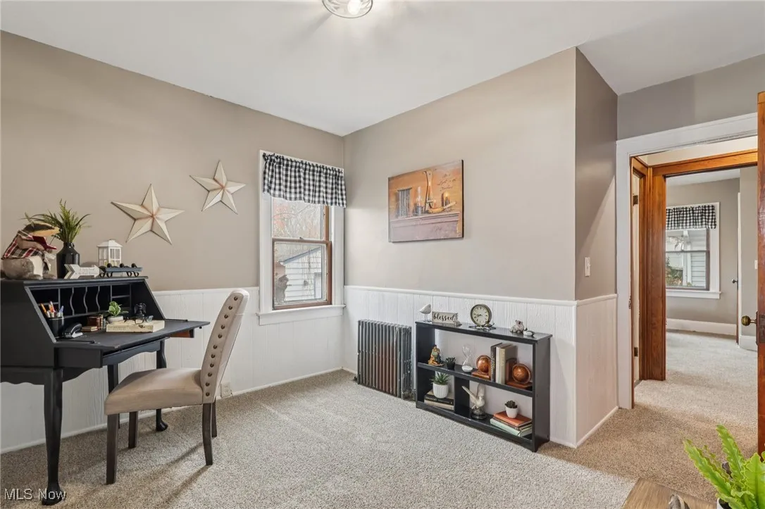Carpeted office space featuring radiator and wainscoting