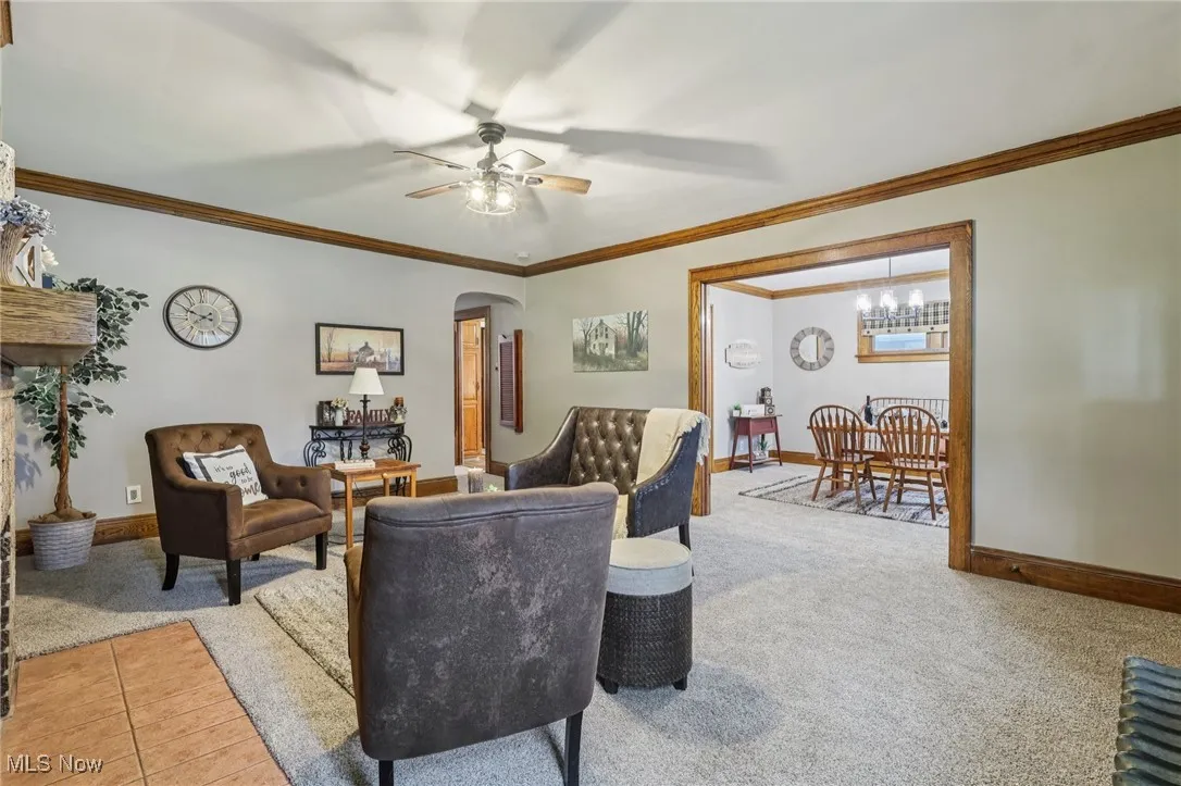 Living room with crown molding, arched walkways, carpet floors, and ceiling fan