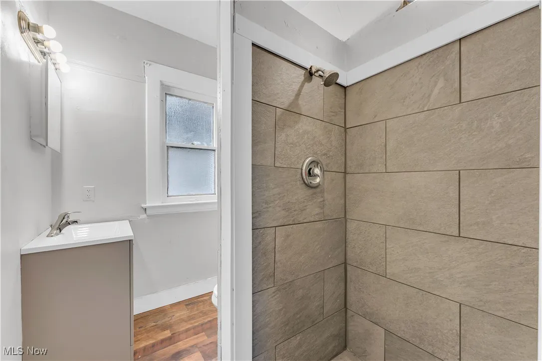 Full bath featuring vanity, a tile shower, and wood finished floors