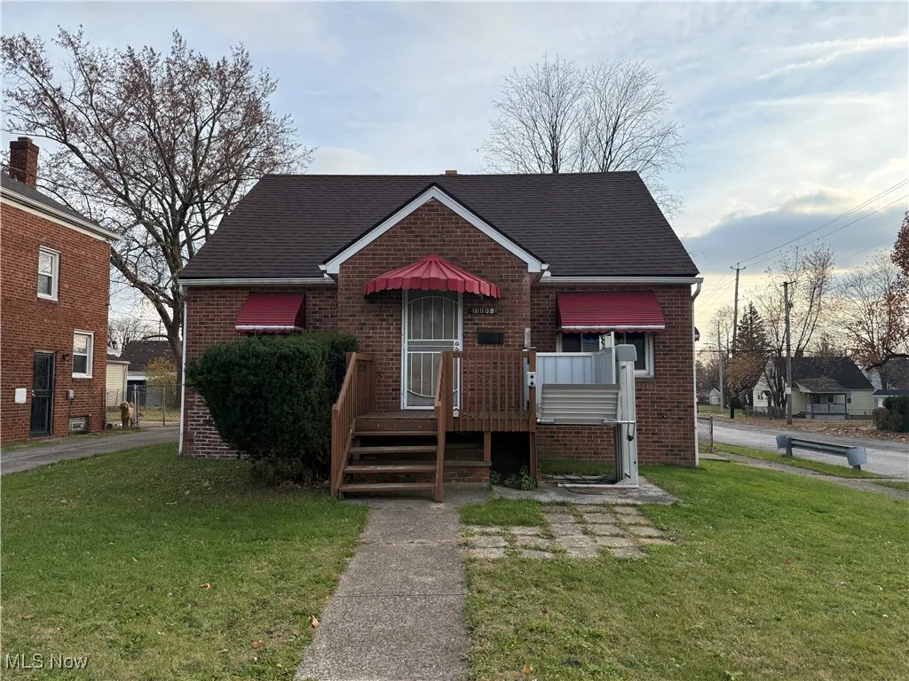 Bungalow-style house with a front lawn, brick siding, roof with shingles, and a deck