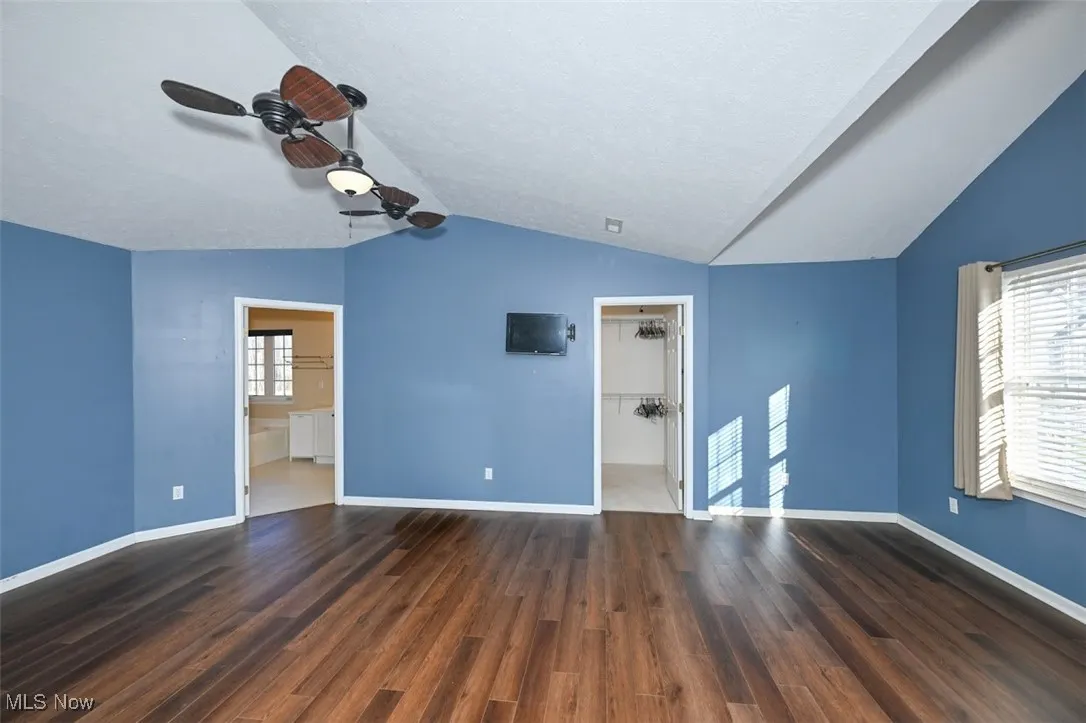 Primary bedroom featuring a walk in closet, dark wood-style flooring, lofted ceiling, ceiling fan, and a textured ceiling