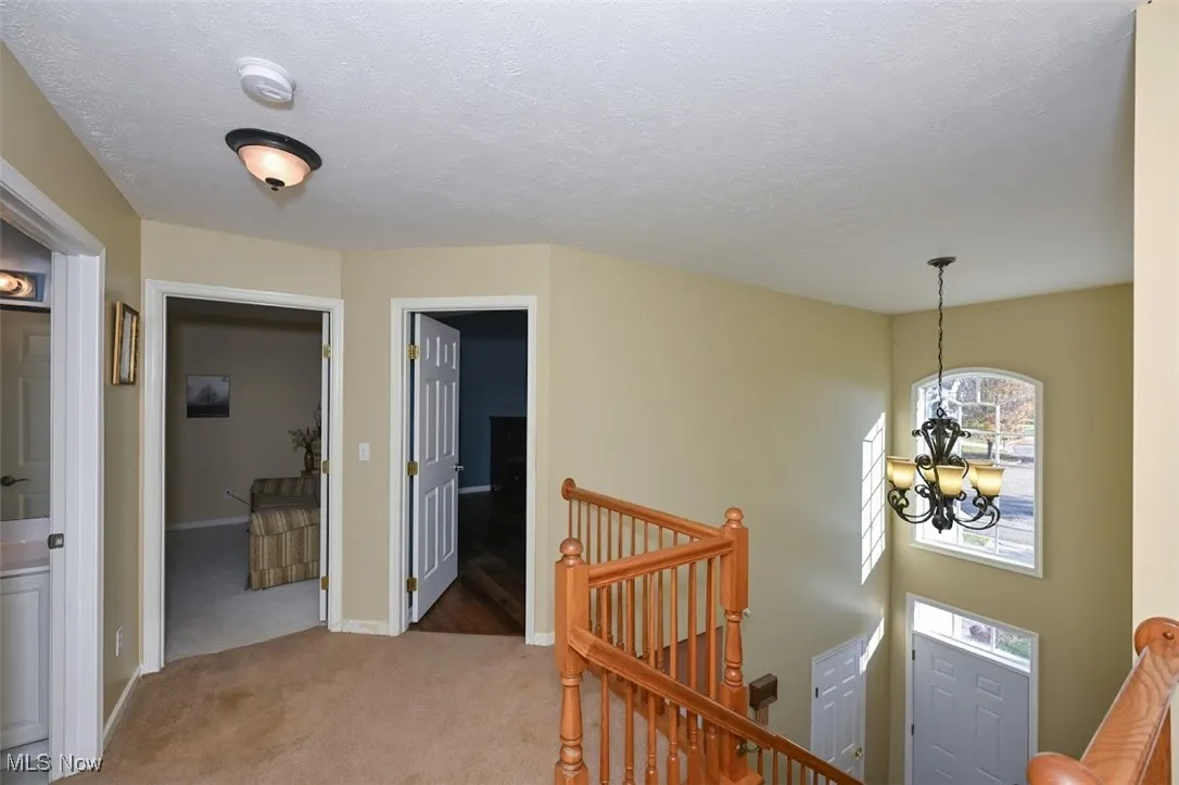 Hall with an upstairs landing, light carpet, a chandelier, and a textured ceiling