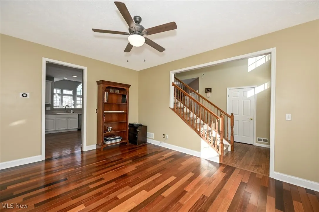 Unfurnished living room with stairway, dark wood-type flooring, and a ceiling fan