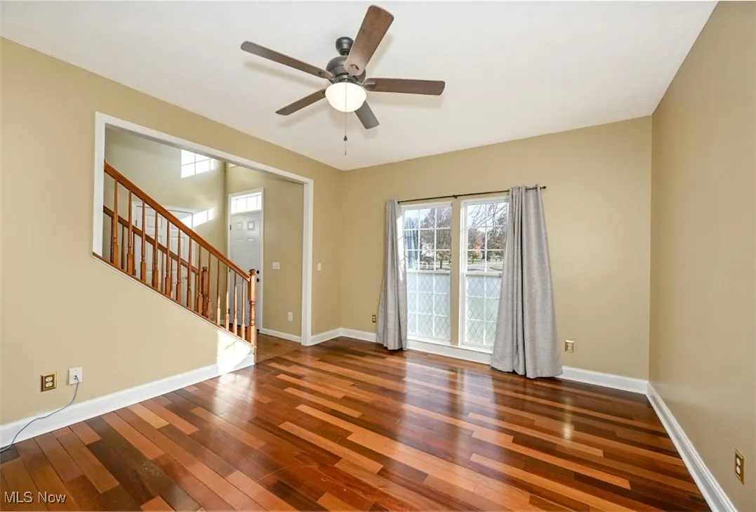 Spare room featuring stairway, dark wood-style flooring, and a ceiling fan