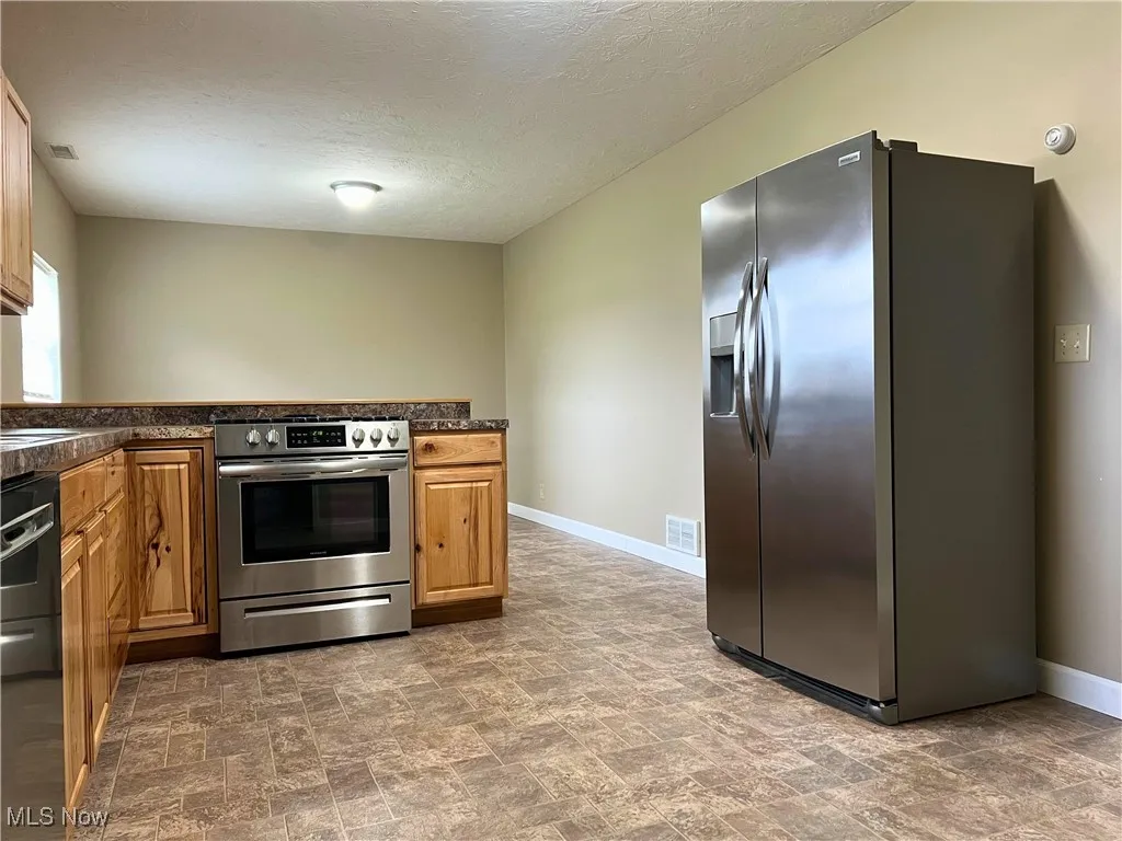 Kitchen with dark countertops, appliances with stainless steel finishes, stone finish flooring, a textured ceiling, and a peninsula