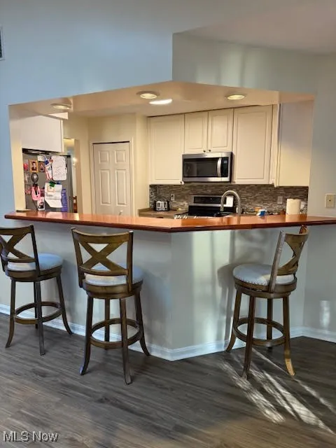 Kitchen with a breakfast bar, appliances with stainless steel finishes, a peninsula, white cabinetry, and dark wood-style flooring