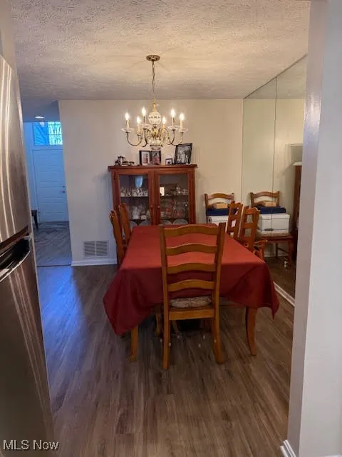 Dining room with a chandelier, dark wood-style floors, and a textured ceiling