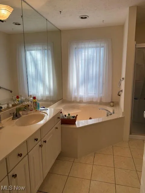 Bathroom featuring a whirlpool tub, vanity, a stall shower, light tile patterned floors, and a textured ceiling