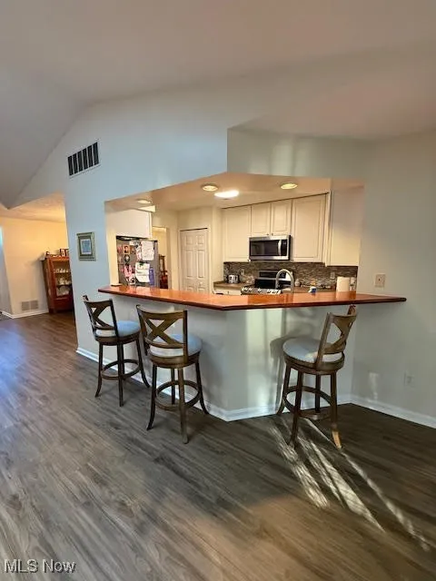 Kitchen with a breakfast bar, appliances with stainless steel finishes, a peninsula, dark wood-style floors, and lofted ceiling