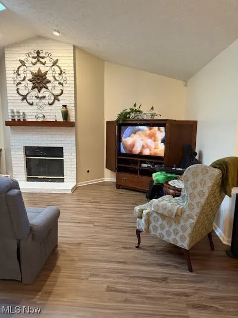 Living room with vaulted ceiling, a fireplace, light wood-style floors, and a textured ceiling